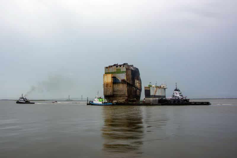 Multiple tugs move a dry-dock barge loaded with Section Six of the Golden Ray wreck to a response facility south of Mayor’s Point Terminal on Saturday.