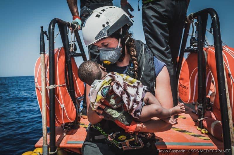 A Rescuer with a baby in her hands onboard