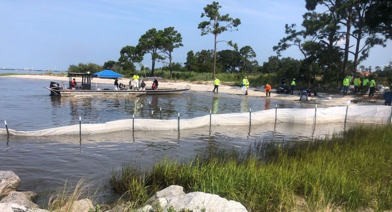 A shoreline clean-up team installs a temporary fence lined with sorbent material to capture any floating residual oil during tidal cycles near the Wylie Street public beach access on Tuesday.