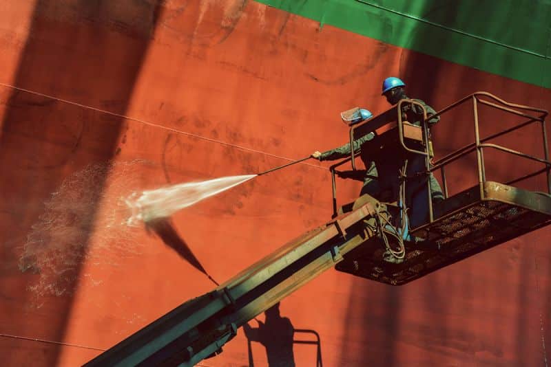 Two woker Washing or cleaning by high pressure water jet. Cargo ship external wall cleaning shell are doing these people at shipyard in Thailand on retro filter tone.